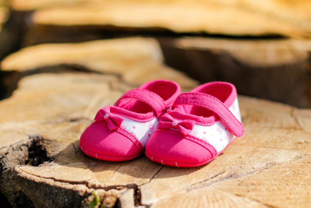 Cute pink baby shoes placed on a textured wooden surface, perfect for newborn photo themes.